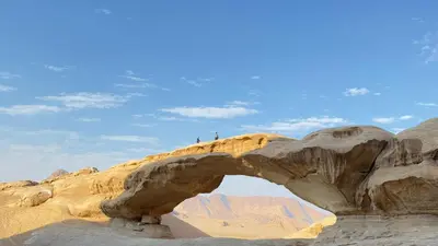 an arch in the desert with two people standing on it at Wadi Rum famous luxury camp in Wadi Rum
