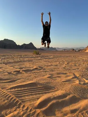 a man jumping in the air in the desert at Wadi Rum murahf camp in Wadi Rum