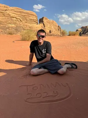 a man sitting on the ground in the desert at Wadi Rum murahf camp in Wadi Rum