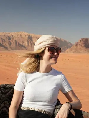 a woman wearing sunglasses sitting in the desert at RUM DESERT BREEZE lUXURY CAMP&JEEP TOUR in Wadi Rum