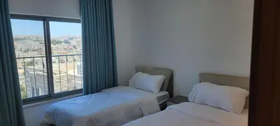 two beds in a room with a large window at العبد للشقق الفندقية in Amman