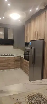 a kitchen with a stainless steel refrigerator and wooden cabinets at شقة مفروشة للايجار دوار المشاغل شارع الأقصى in Amman