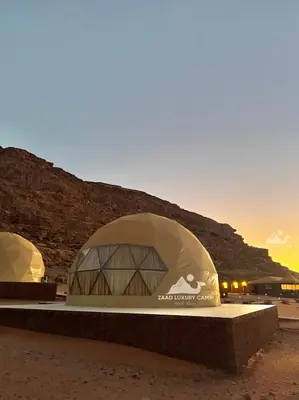 a building in the desert with the sunset in the background at Wadi Rum ZAAD luxury Camp in Wadi Rum