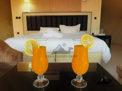 three glasses of orange juice on a table in front of a bed at Wadi Rum ZAAD luxury Camp in Wadi Rum