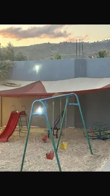 a play area with swings and a large canopy at منتجع ومزرعة برجيل السد in Ballās