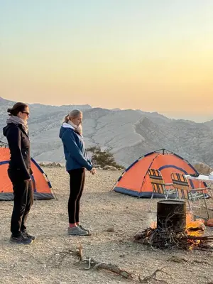 two women standing next to tents and a campfire at Dana Hiking Camp - Dana Nature Reserve in Dana