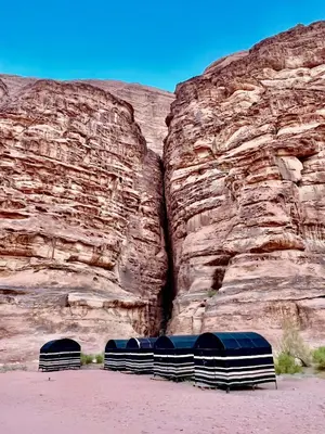 a group of beds in front of a rock wall at Wanderlust Jordan Camp in Wadi Rum