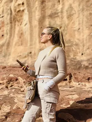a woman holding a gun while standing on a cliff at calm Rum in Wadi Rum