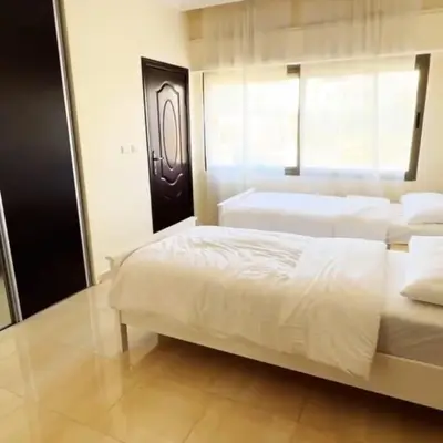 a bedroom with two white beds and a window at Badr in Amman