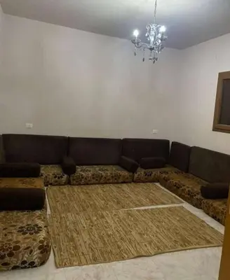 a living room with a brown couch and a chandelier at kazbon House in Al Hāshimīyah