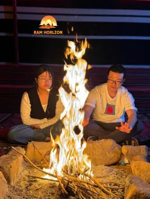 a man and a woman sitting around a fire at RAM HORlZON LUXURY CAMP in Wadi Rum