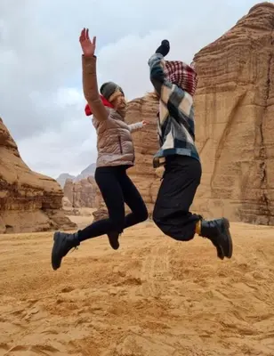 two people jumping in the air in the desert at Al-Faris Camp in Disah