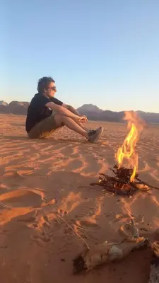 a woman sitting on the ground next to a bonfire in the desert at جمال رم in Aqaba