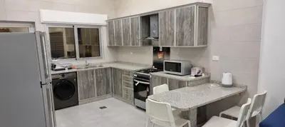 a kitchen with wooden cabinets and a table and a microwave at Cozy, Newly Furnished & Budget Friendly Apartment in Amman
