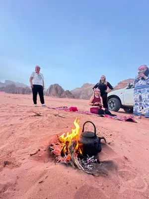 a group of people standing around a campfire on the beach at Desert Star Camp in Wadi Rum