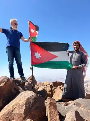 two men standing on top of a mountain holding a flag at Ruby Orbit Wadi Rum in Wadi Rum