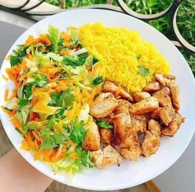 a white plate of food with chicken and rice at 77 apartment in Abū aş Şalīḩ