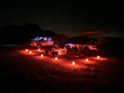 a group of people sitting next to a truck with candles at Sands of time desert camp in Wadi Rum