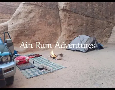 a tent and a fire in the sand with the words aim run adventures at مغامرات عين رم in Wadi Rum