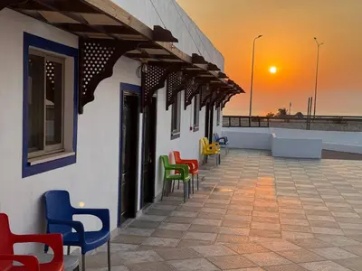a row of colorful chairs on a building with the sunset at Camel Dive Club By The Sea Inn in Jurf ad Darāwīsh
