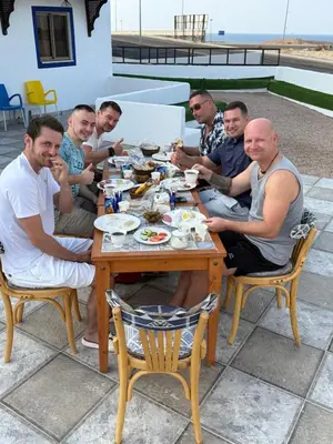 a group of men sitting around a table eating food at Camel Dive Club By The Sea Inn in Jurf ad Darāwīsh