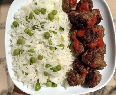 a white plate with rice and meatballs and peas at ام القطين لونج in Umm al Qiţţayn
