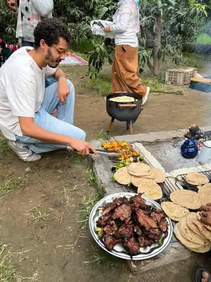 a man sitting next to a grill with a plate of food at ام القطين لونج in Umm al Qiţţayn