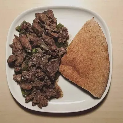 a plate of food with a piece of bread and meat at ام القطين لونج in Umm al Qiţţayn