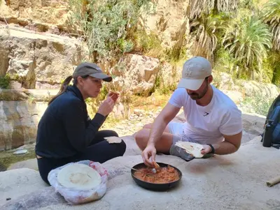 a man and woman sitting on a rock eating food at Dana Village experience hotel in Dana