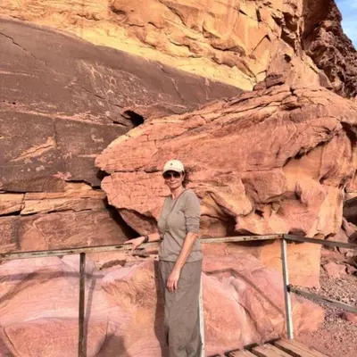 a woman standing in front of a rock wall at وادي رم in Jurf ad Darāwīsh