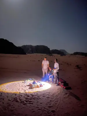 a group of three people standing around a fire on the beach at Bedouin Luxury Camp in Wadi Rum