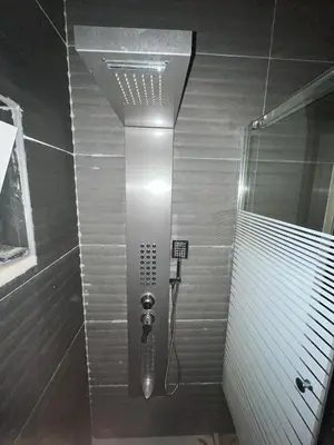 a shower in a bathroom with a light on the wall at Family-Friendly Garden Stay in Jurf ad Darāwīsh