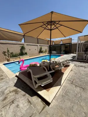 a pool with chairs and an umbrella and a pink flamingo at Oia chalet in Ash Shāghūr