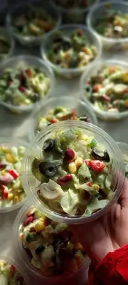 a person holding a bowl of salad in front of plates of food at الصدقه ان in Aş Şadaqah