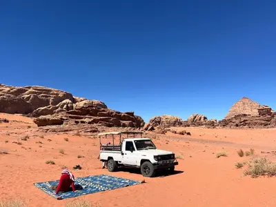 a white truck parked in the desert with a blanket at Wadi Rum Cave Experience in Wadi Rum