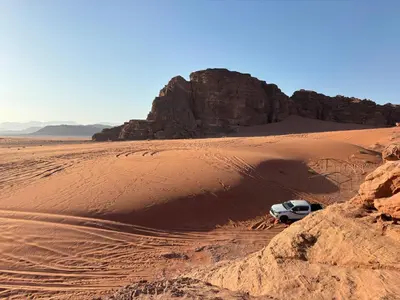a white car parked in the desert at Wadi Rum Cave Experience in Wadi Rum