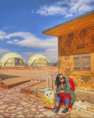 a woman sitting in front of a building with a suitcase at Wadi rum camp hamod in Wadi Rum