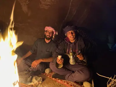 two men are sitting next to a fire at Wadi Rum Starlit in Wadi Rum