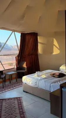 a bedroom with a bed and a large window at Tarf Wadi Rum Luxury Camp & Jeep Tours in Wadi Rum