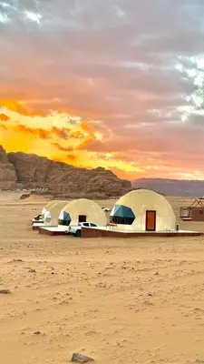 two domes in the desert with the sunset in the background at Tarf Wadi Rum Luxury Camp & Jeep Tours in Wadi Rum