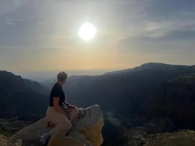a person sitting on a rock looking at the sun at Dana Village lodge and Camp-Wadi Dana Eco camp in Dana