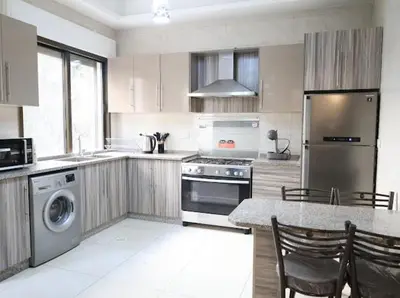 a kitchen with stainless steel appliances and a table with chairs at Rams Der Ghbar 3BR cozy Apt in Amman
