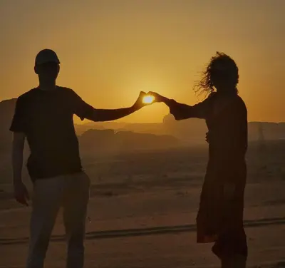a man and woman standing on the beach at sunset at SAHARA ECHO CAMP& Tour in Wadi Rum