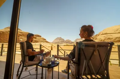 a man and a woman sitting in chairs on a balcony looking at the desert at Moon night camp in Disah