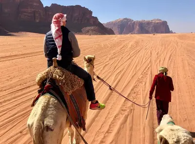 a woman riding a camel in the desert with two dogs at Adventure Nights Camp in Wadi Rum