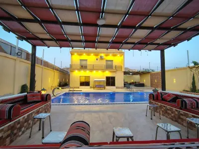 a swimming pool with red chairs and a building at Janna2Villa in Tall al Misţāḩ