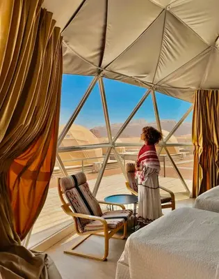 a woman standing in a bedroom with a large window at rum luxury camp in Wadi Rum