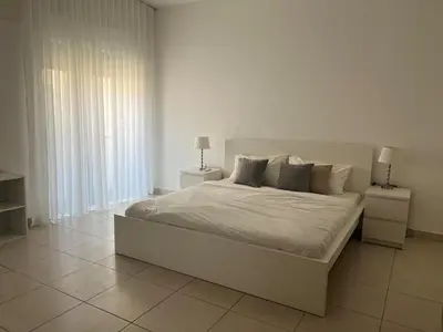 a white bedroom with a large bed with two night stands at Newly refurbished 2-bedroom flat in a compound in Amman
