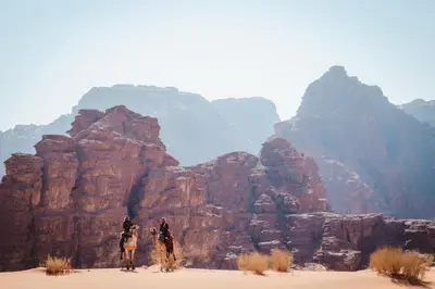 two people riding on horses in the desert at مخيم نجوم رم in Maḩaţţat Dīsah