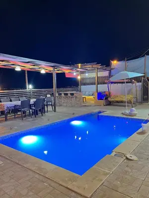 a swimming pool at night with a table and chairs at شاليه بانا جرش in Jerash